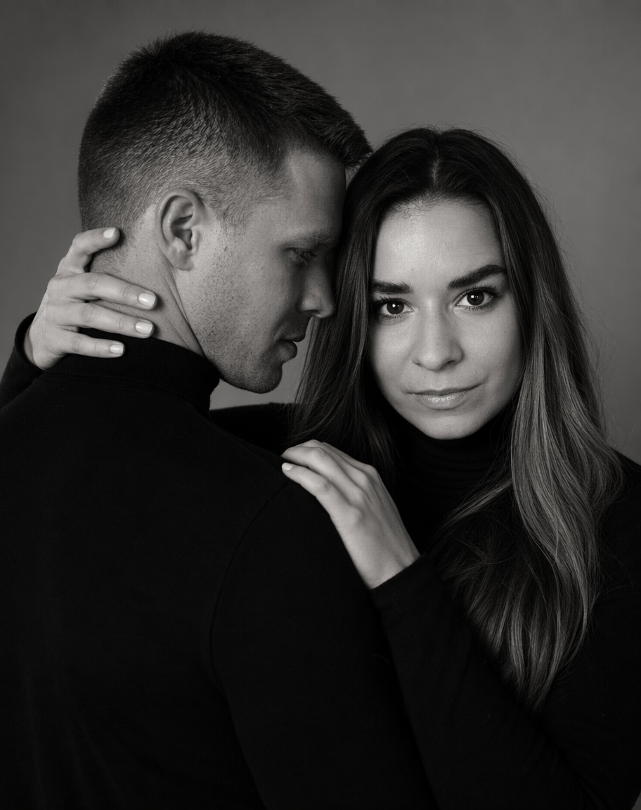 Kobieta w czarnym golfie obejmuje mężczyznę za szyję podczas czarno-białej sesji romantycznej w studio